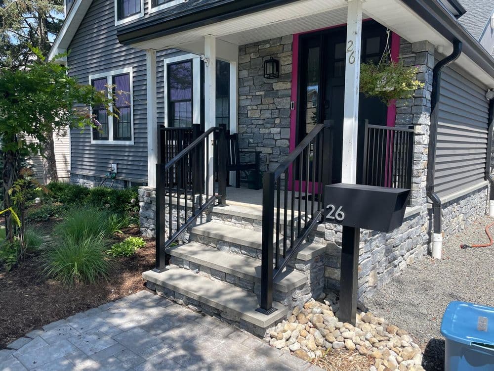 Front entrance of a modern home with stone steps, black railings, and mailbox at number 26.