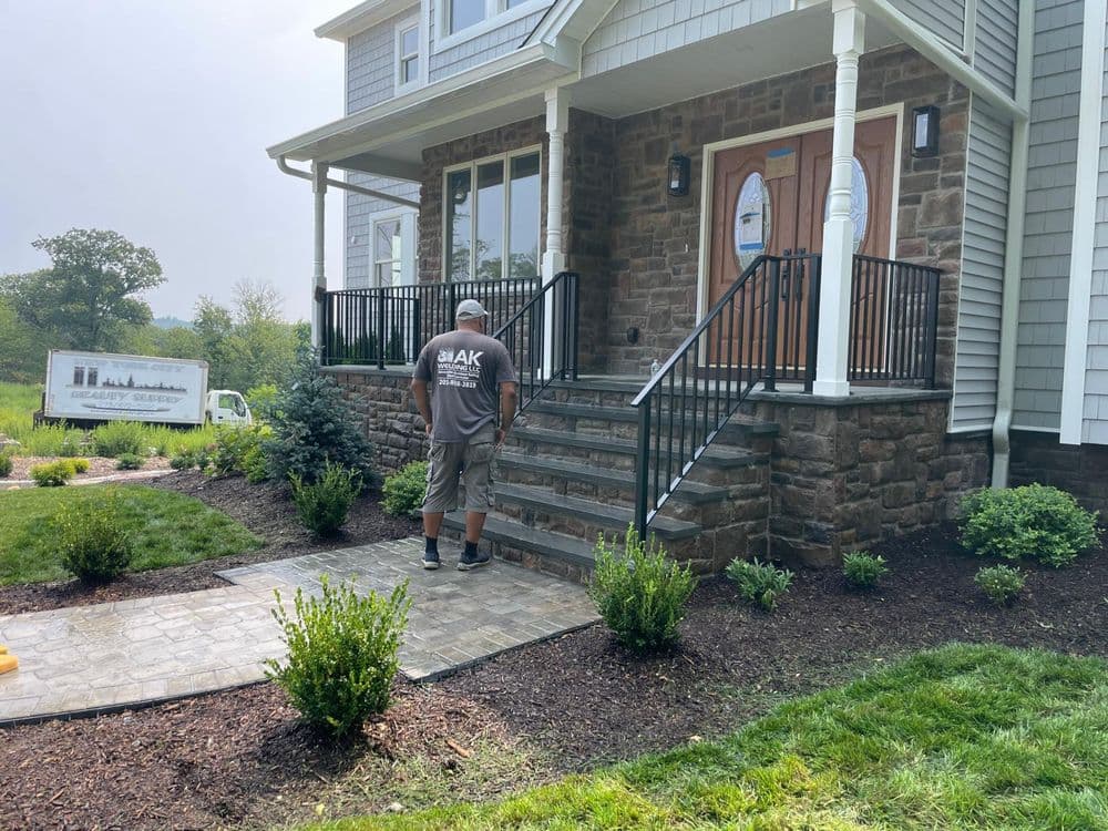 Worker installing stone steps at a residential entrance with landscaping around the home.