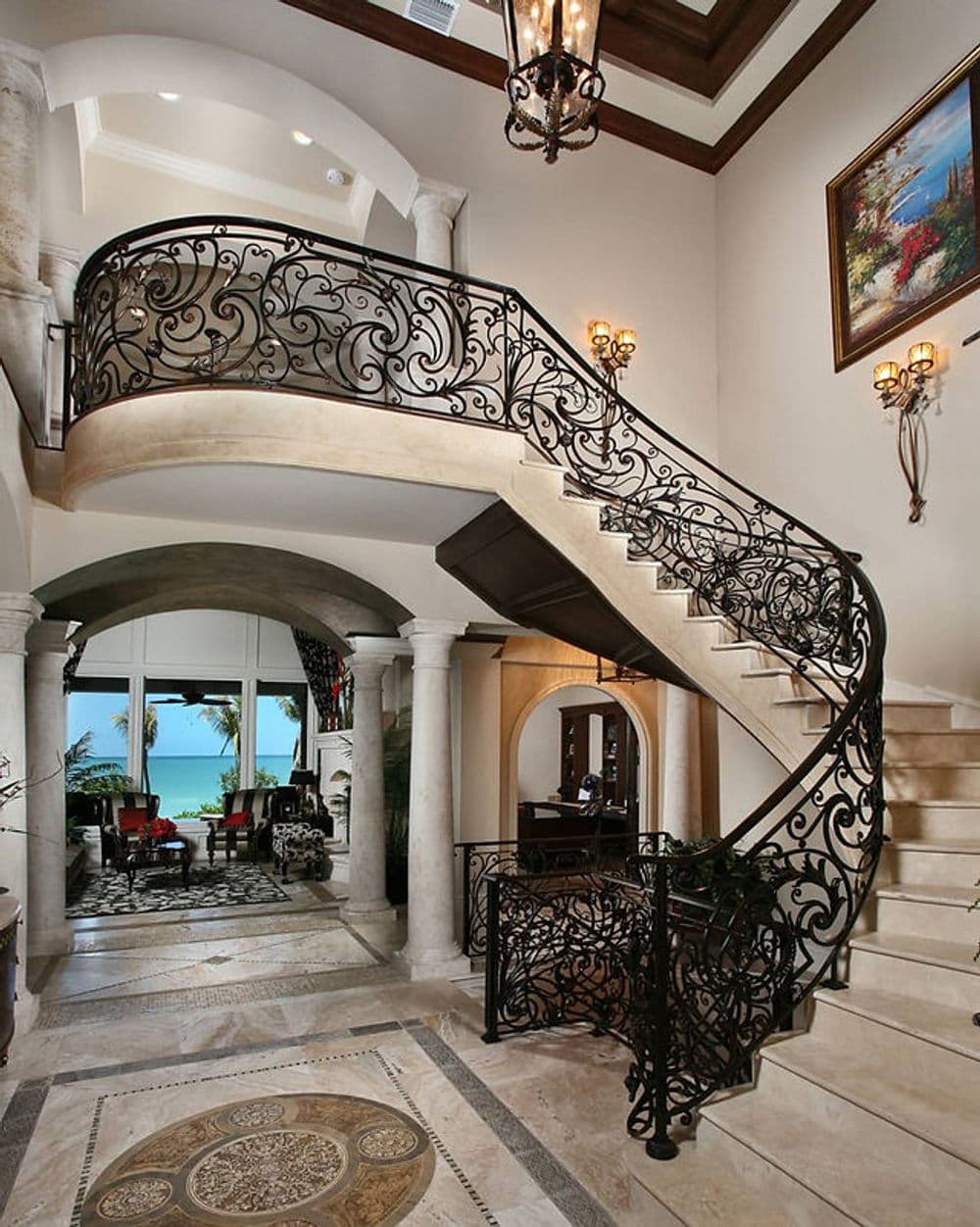 Elegant curved staircase with intricate iron railing in a luxurious entryway. Marble floor details.