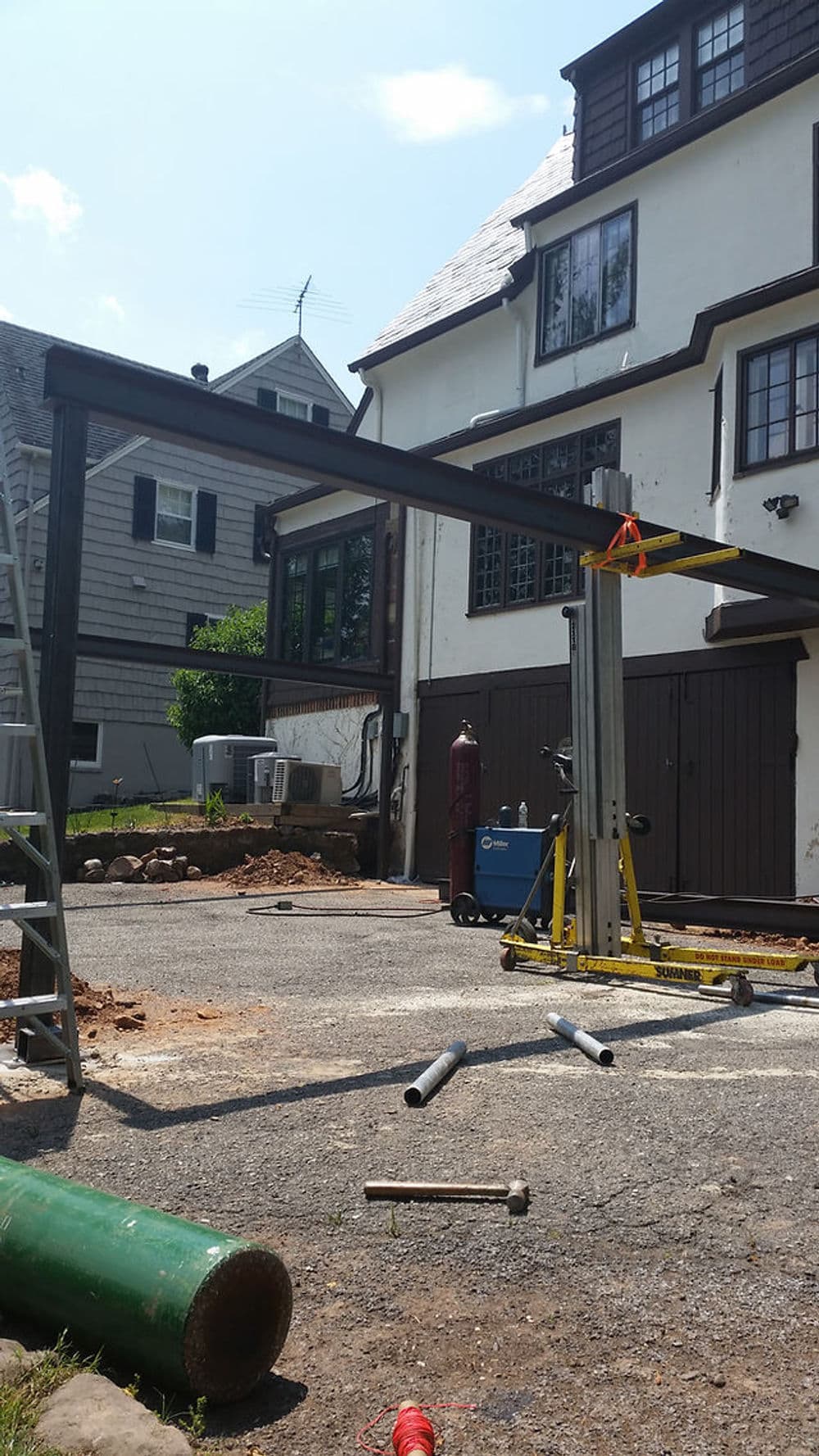 Construction site featuring a metal framework and tools near a house with a modern design.