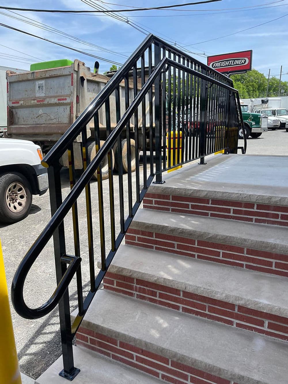 Black metal railing alongside brick stairs leading to a transportation facility.