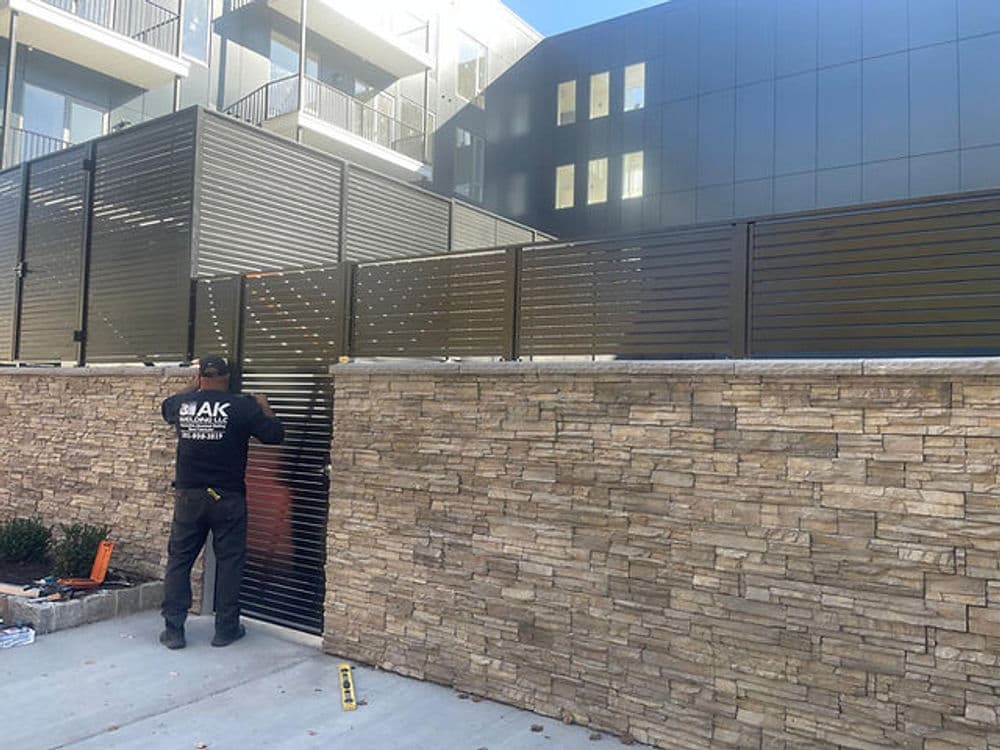 Worker installing modern metal gate at contemporary building with stone wall.