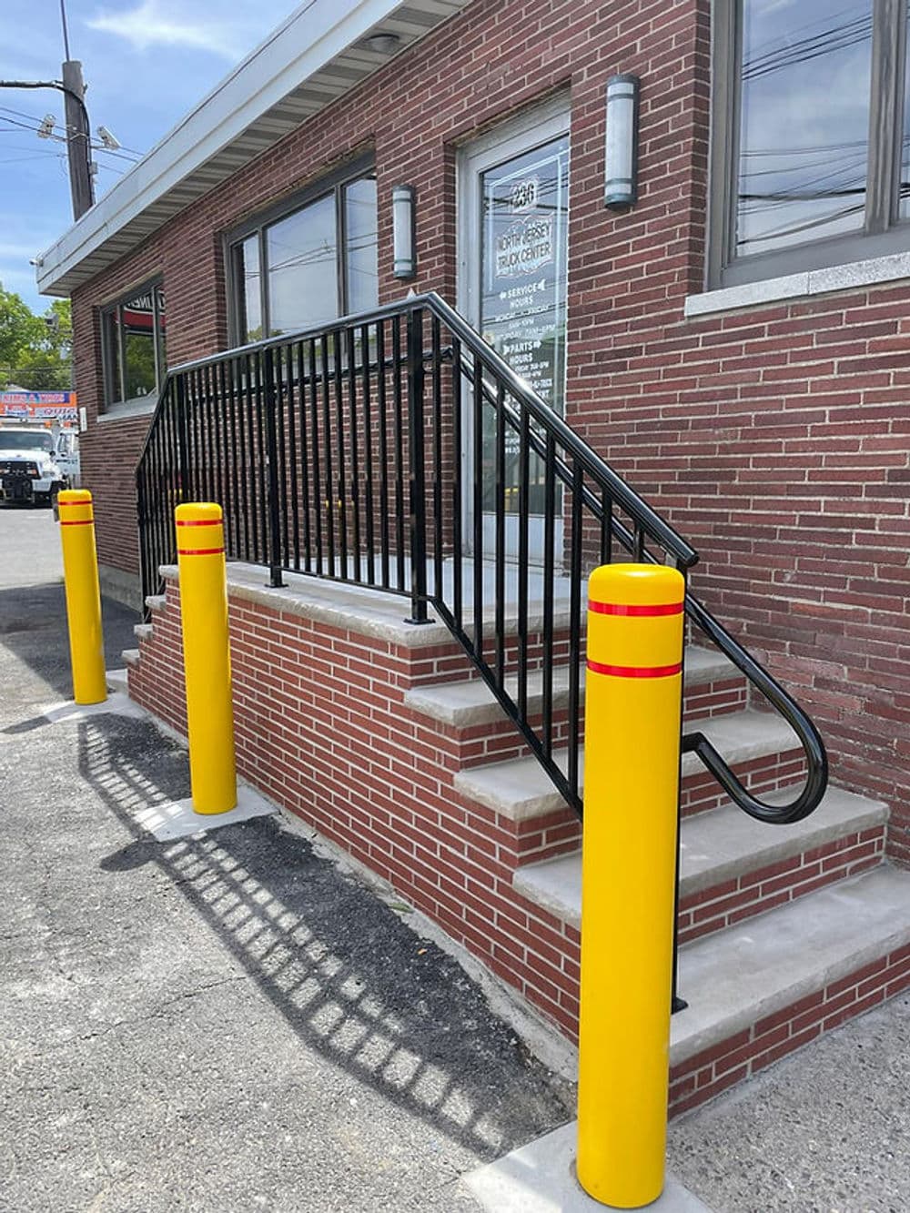 Accessible ramp with black railing beside yellow safety bollards at brick building entrance.