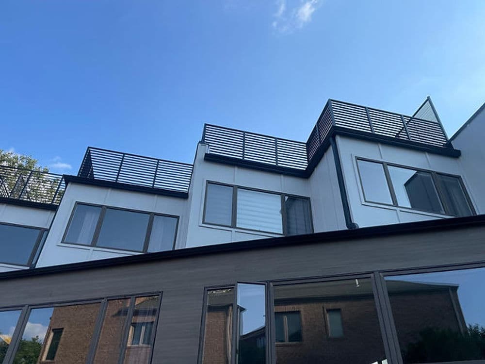 Modern apartment building with large windows and rooftop terrace under blue sky.
