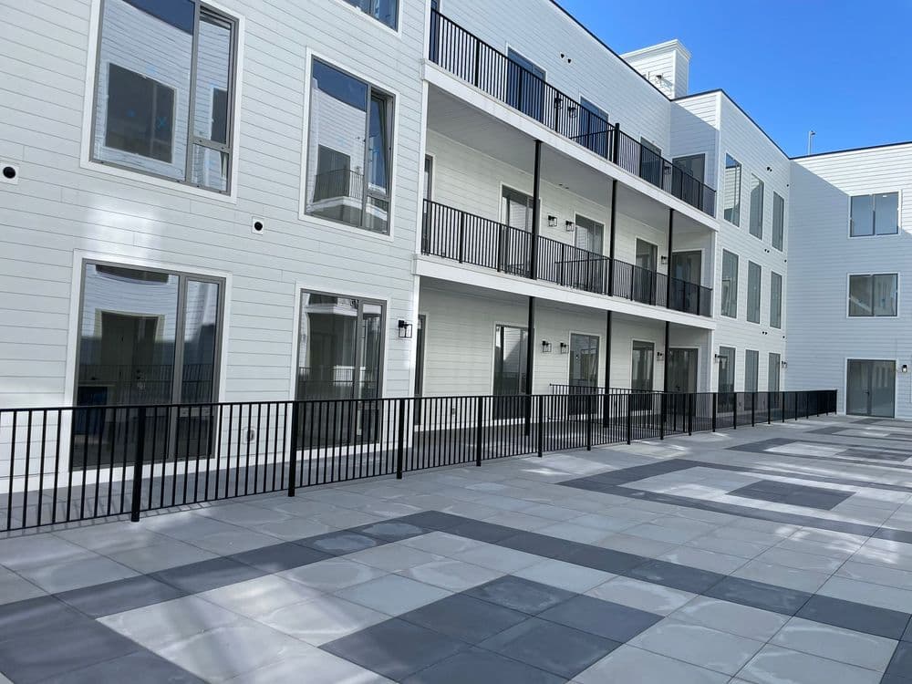 Modern apartment building exterior with balconies and a tiled patio area.