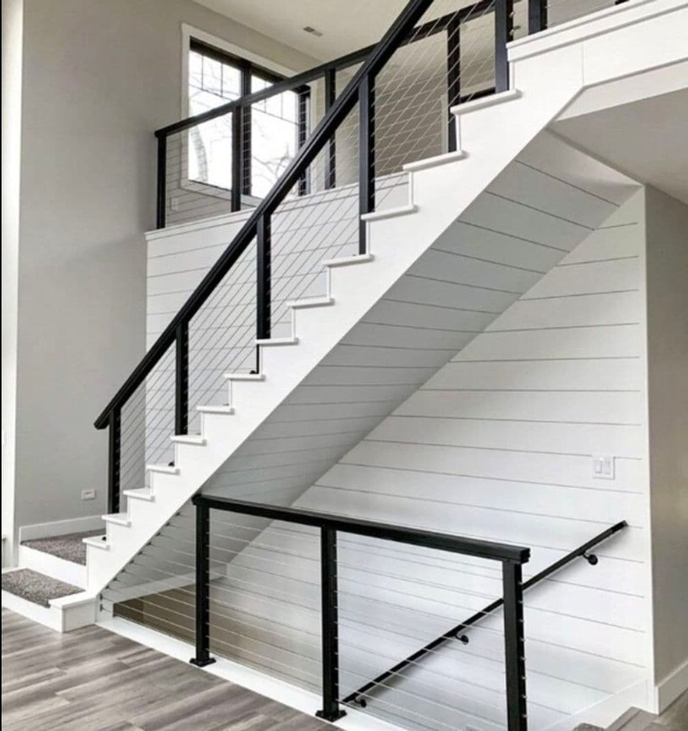 Modern interior staircase with black railing and white shiplap walls in bright space.