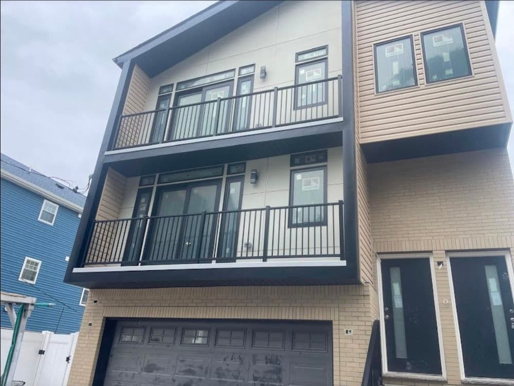 Modern three-story townhouse with balconies and garage in a residential area.