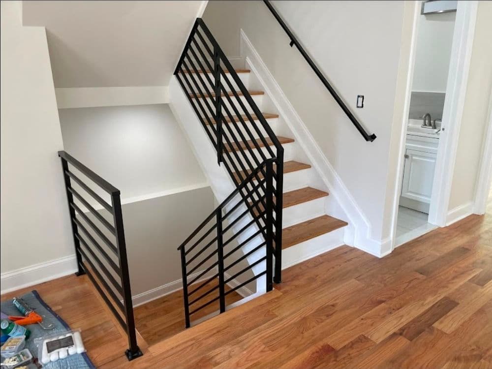 Modern staircase with wooden steps and black metal railing in a light-filled interior.
