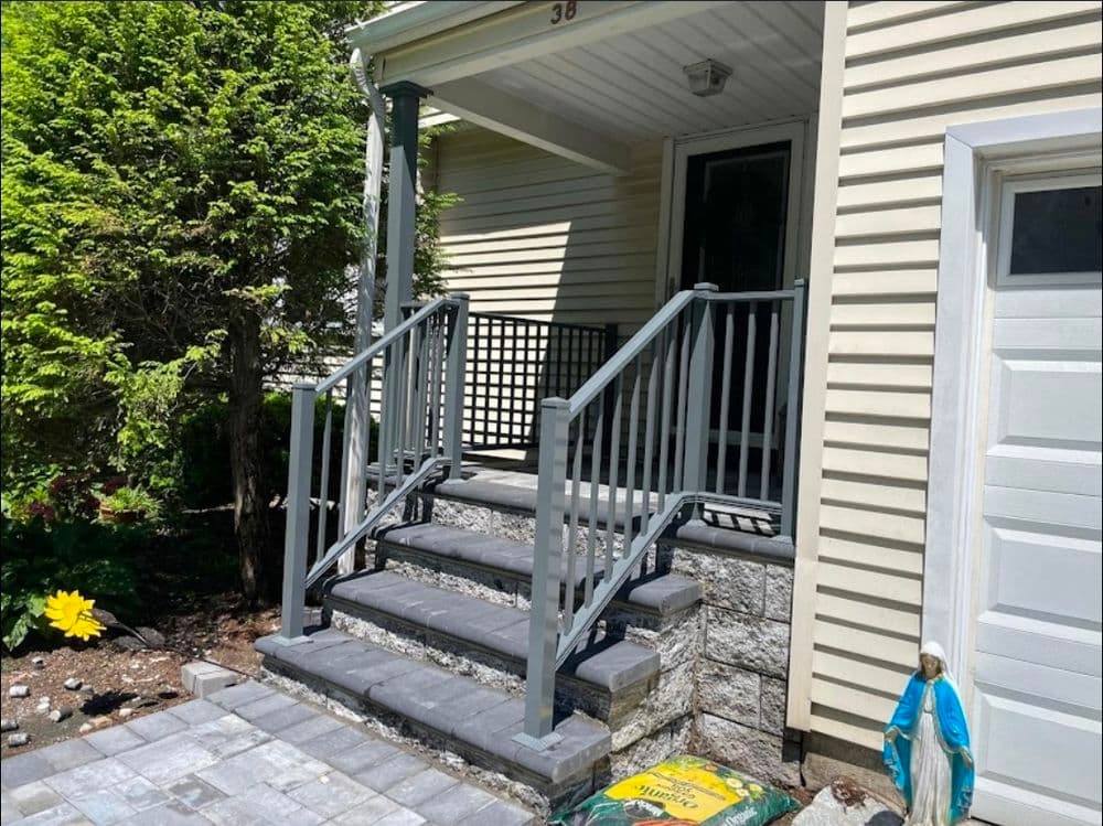 Modern home entrance with gray railings, stone steps, and landscaped flower bed.