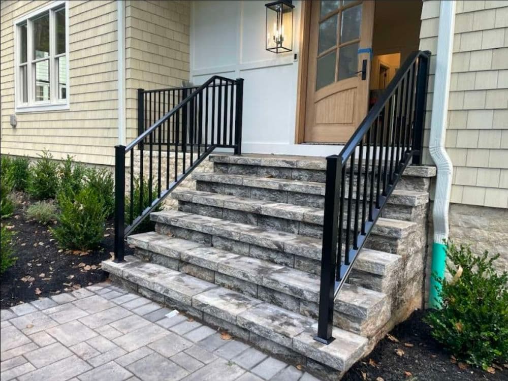 Modern stone steps with black metal railing leading to a house entrance.