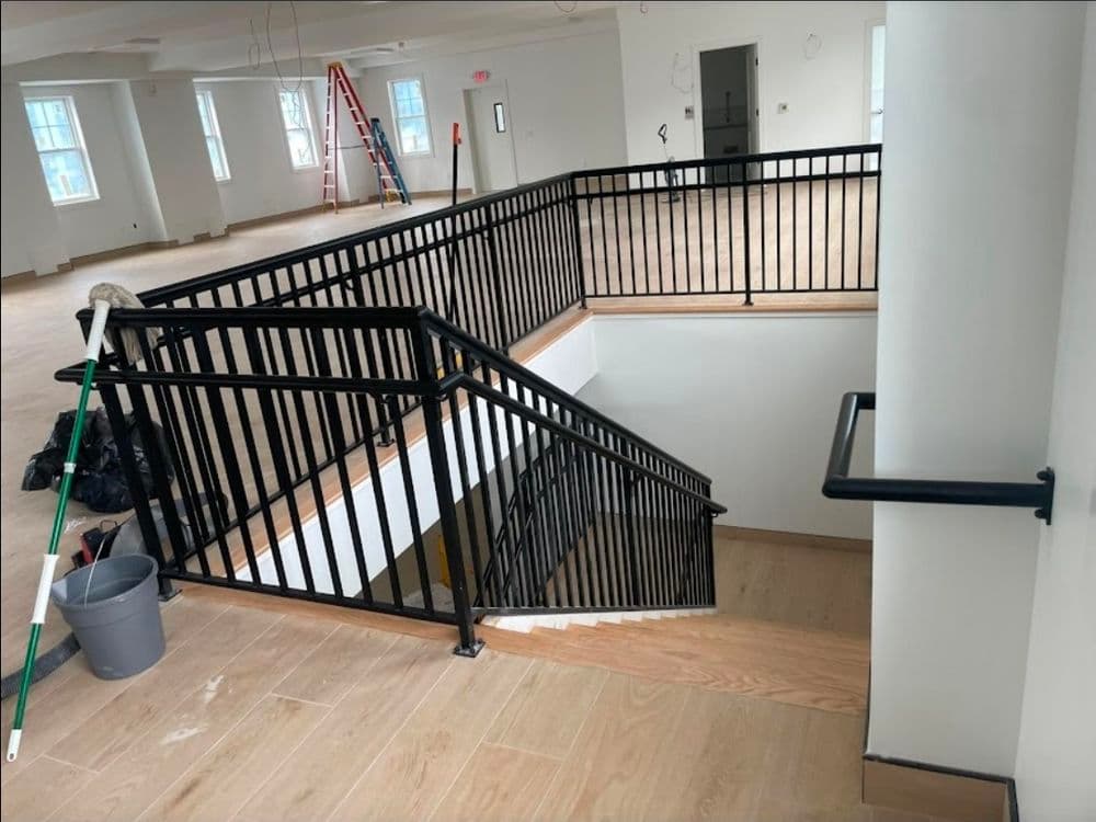 Modern interior staircase with black railing in partially finished room, construction tools nearby.