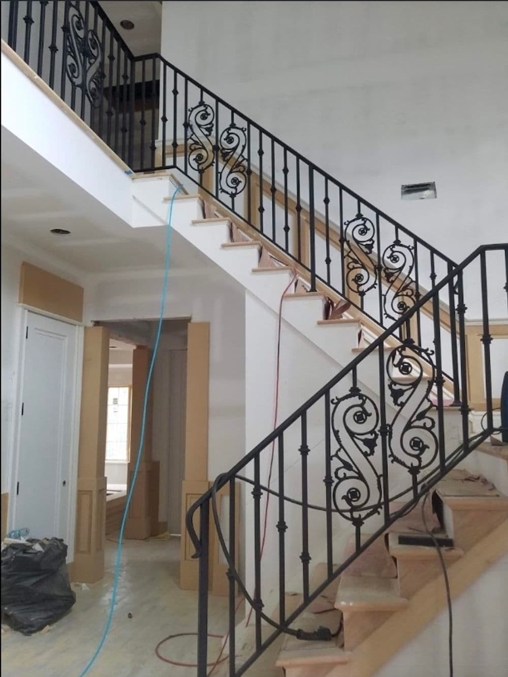 Elegant staircase with black wrought iron railing in a modern interior under renovation.