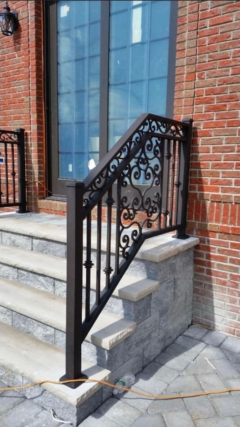 Decorative black metal railing on stone steps leading to a brick house entrance.