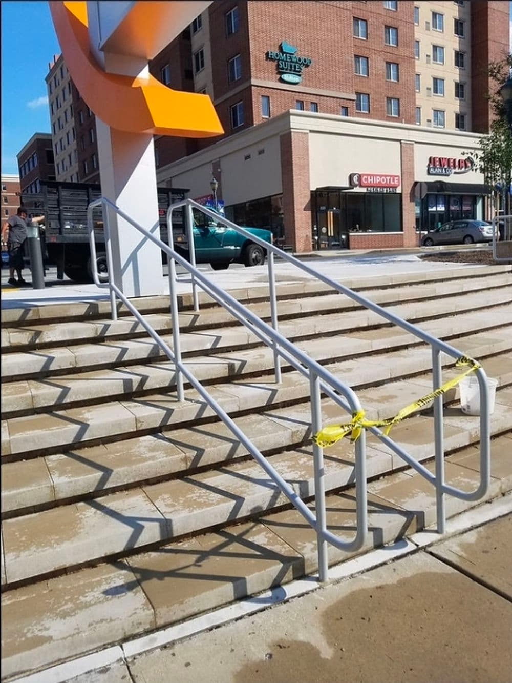 Staircase with railings and caution tape in an urban setting, near shops and hotel.