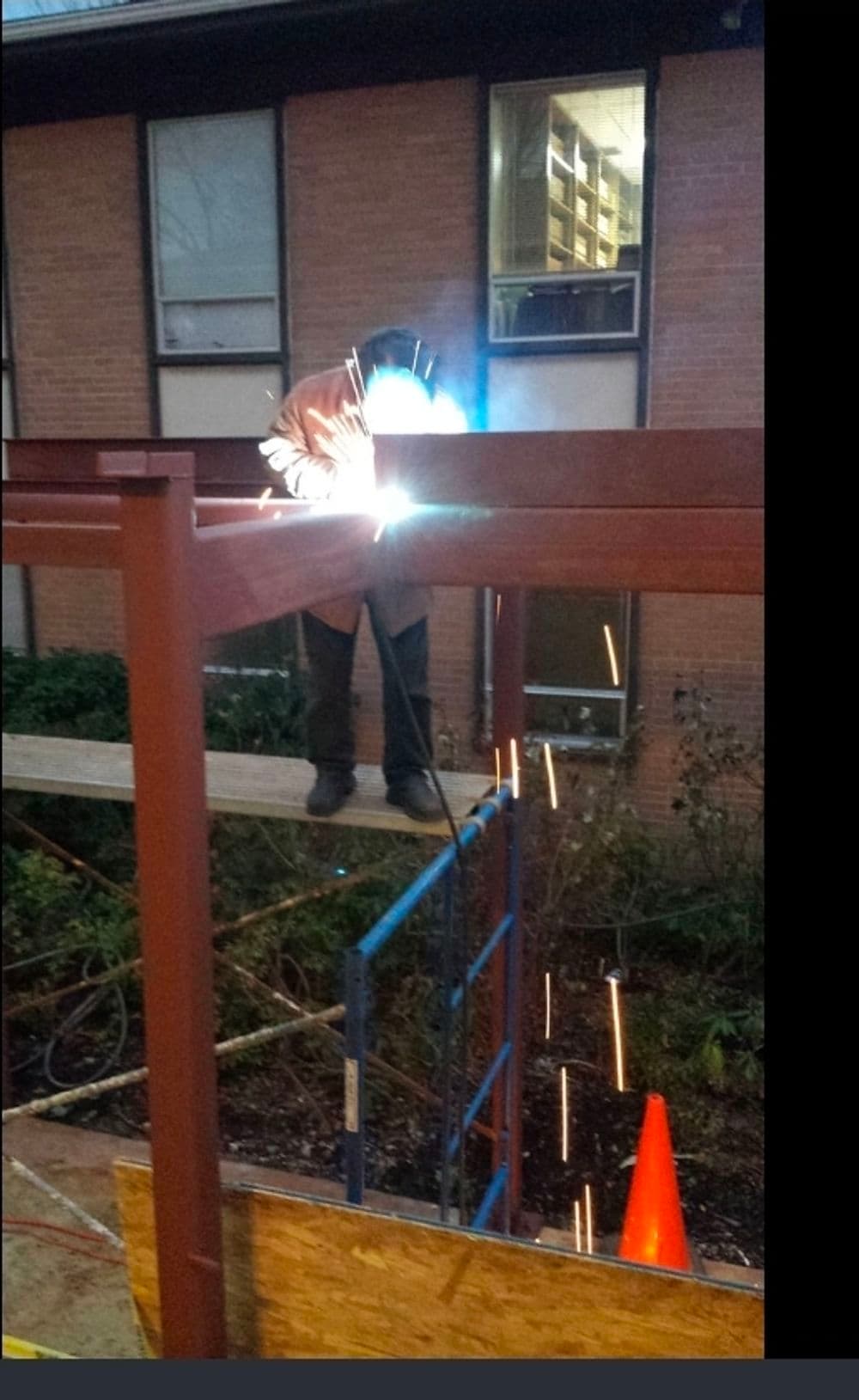 Welder working on a metal frame with sparks flying on a construction site.
