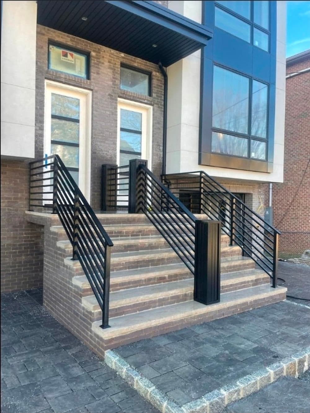 Modern home entrance with black railings and steps, featuring brick and glass design elements.