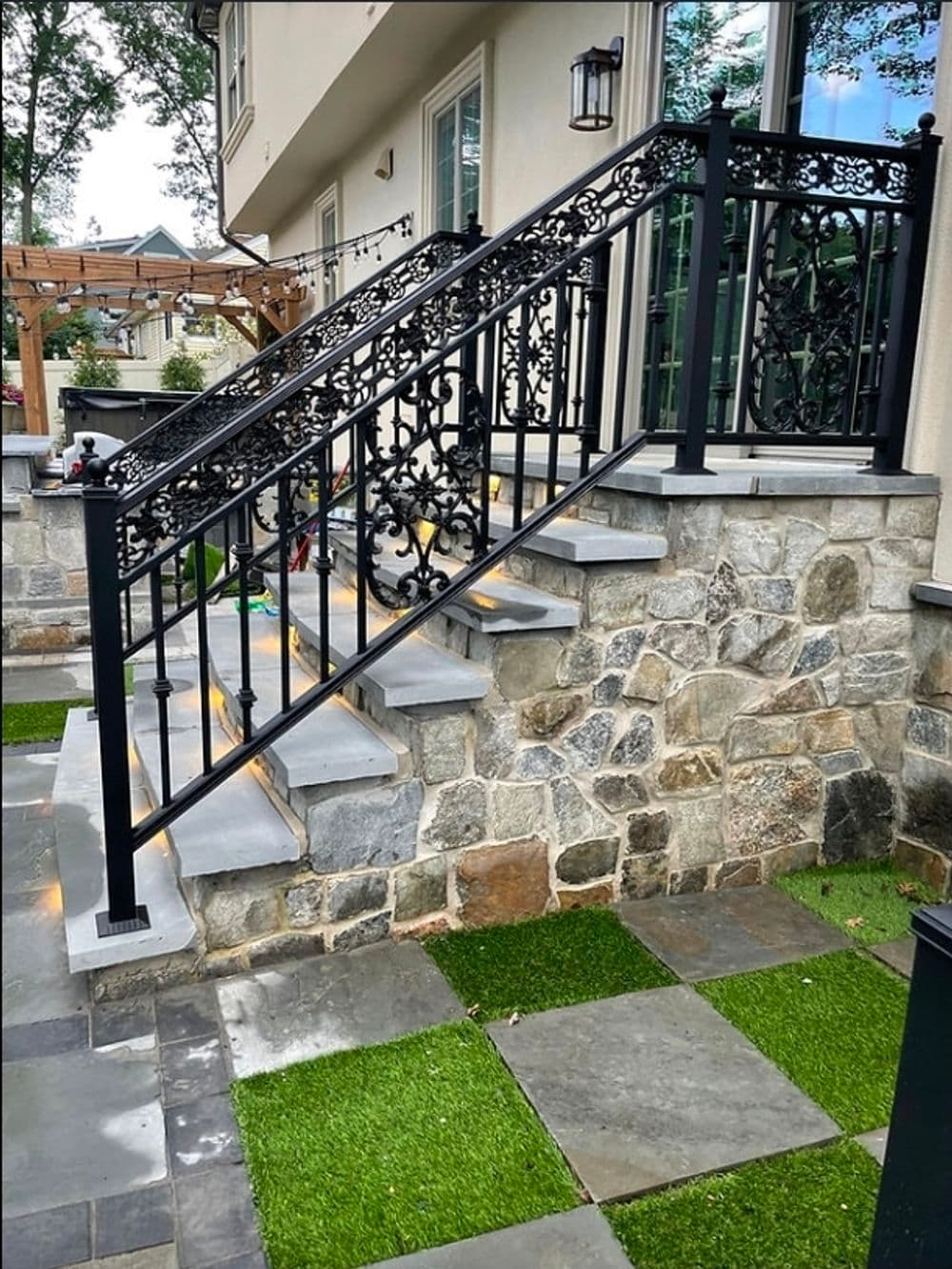 Elegant wrought iron railing on stone stairs leading to a modern house entrance.