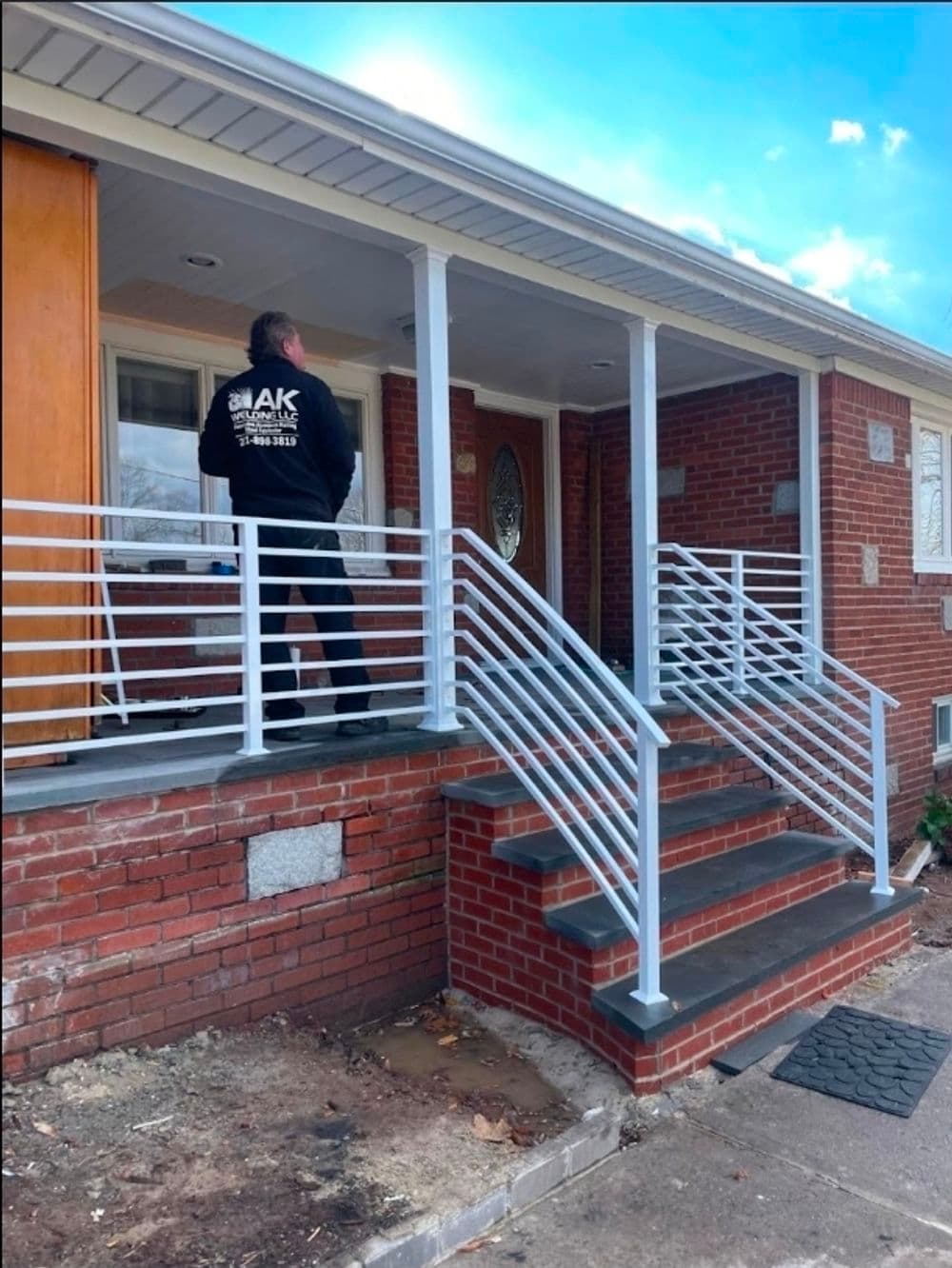 Man standing on a brick porch with modern metal railing and steps leading to a home.
