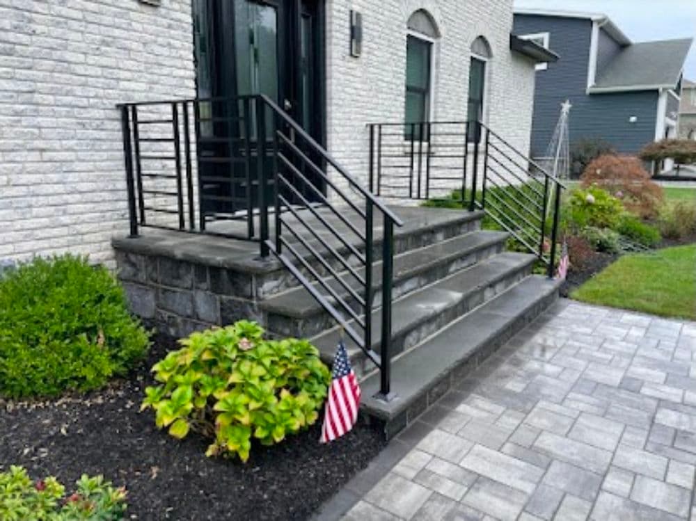 Modern home entrance with black railing and steps, featuring small American flags on the sides.