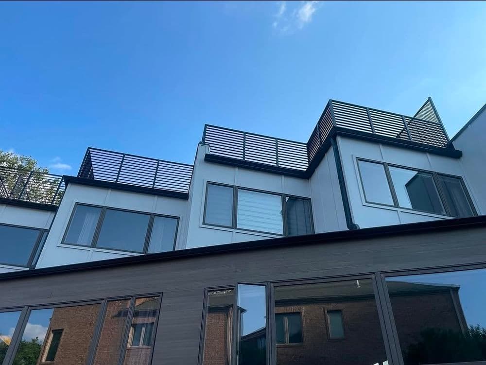 Modern multi-story building with sleek windows and rooftop terrace against a clear blue sky.