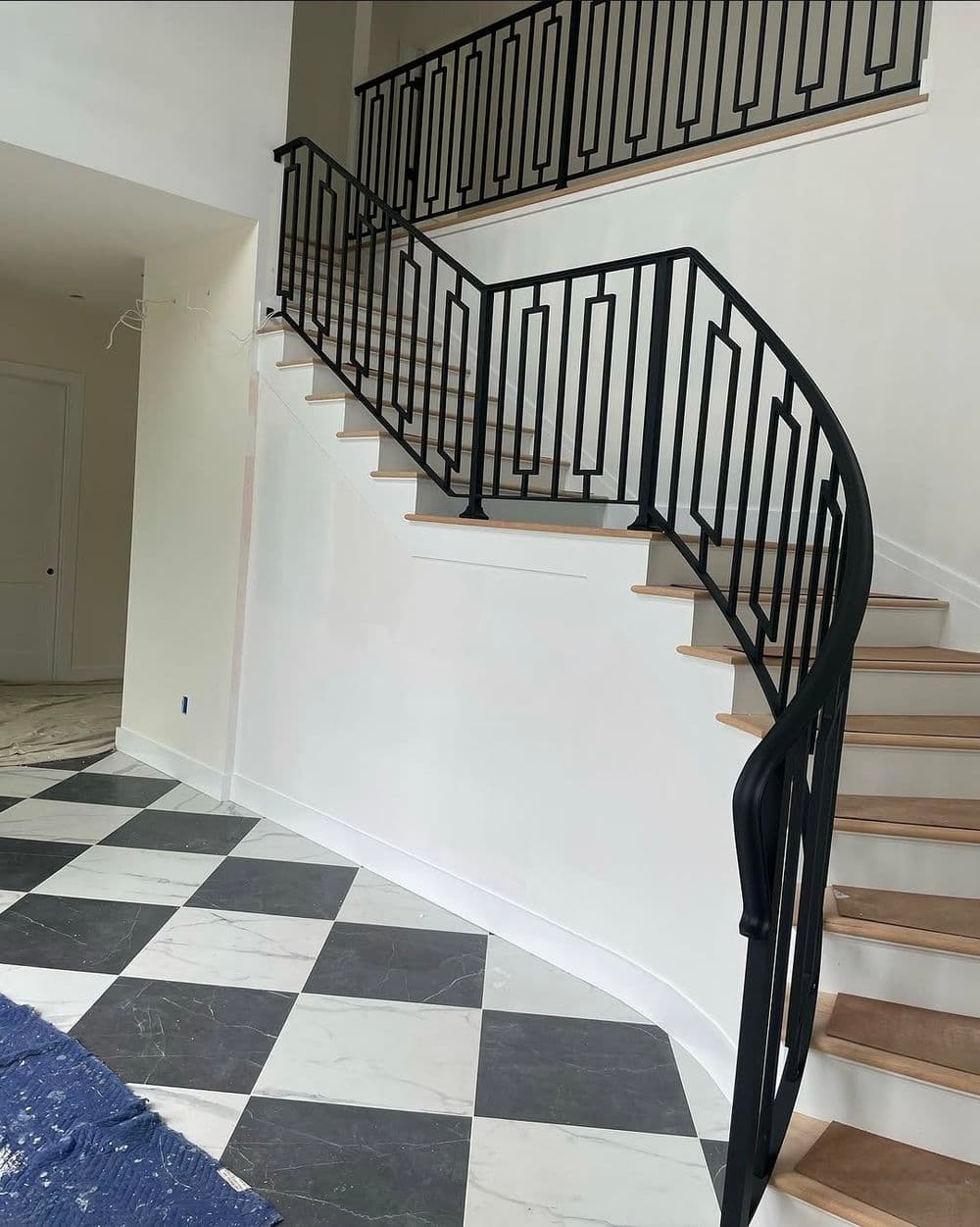 Elegant spiral staircase with black railing in a modern foyer featuring marble and checkerboard flooring.