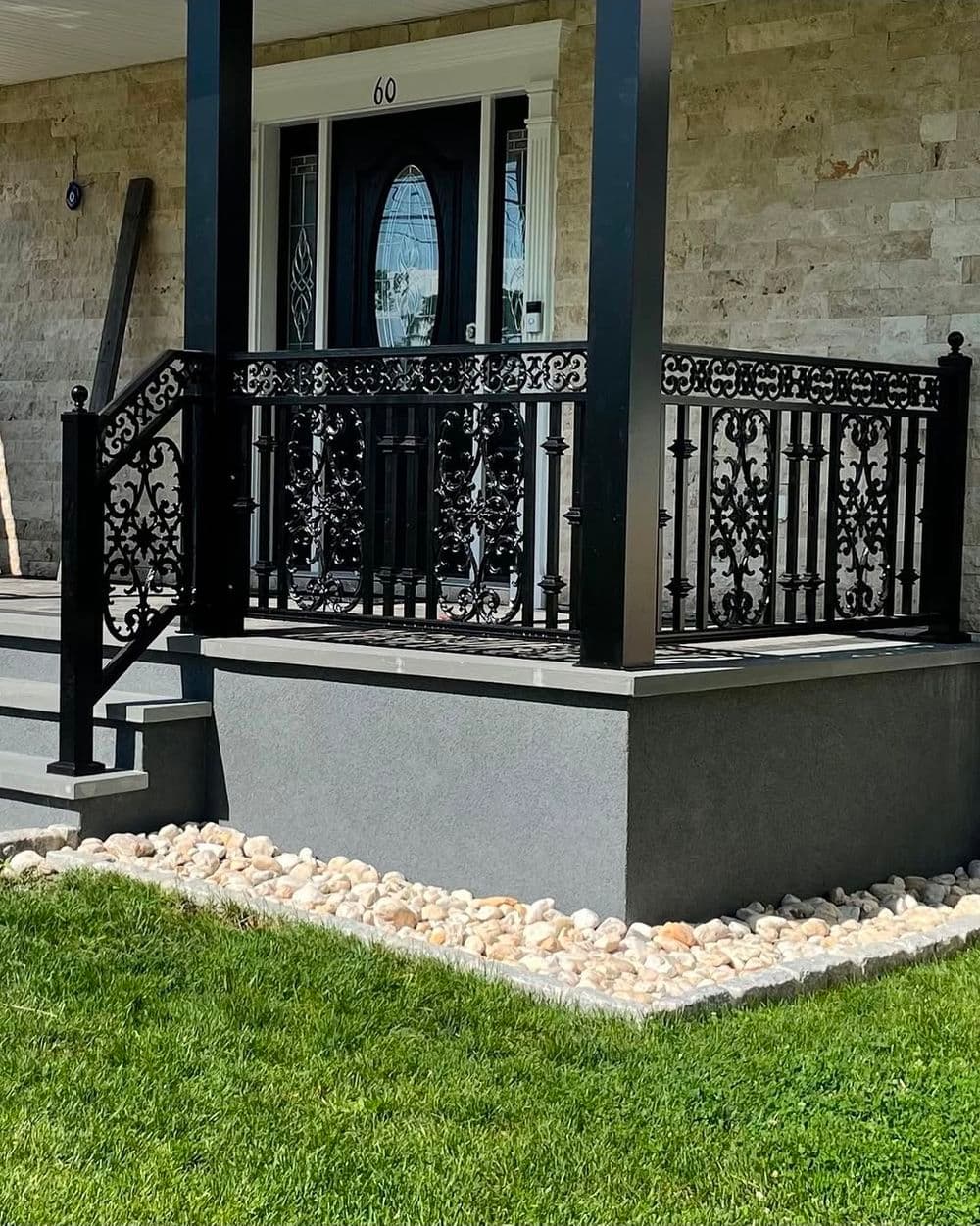 Elegant black wrought iron railing on a modern porch with landscaped stone border.