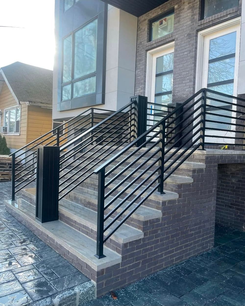 Modern black metal railing and stone steps leading to a contemporary building entrance.