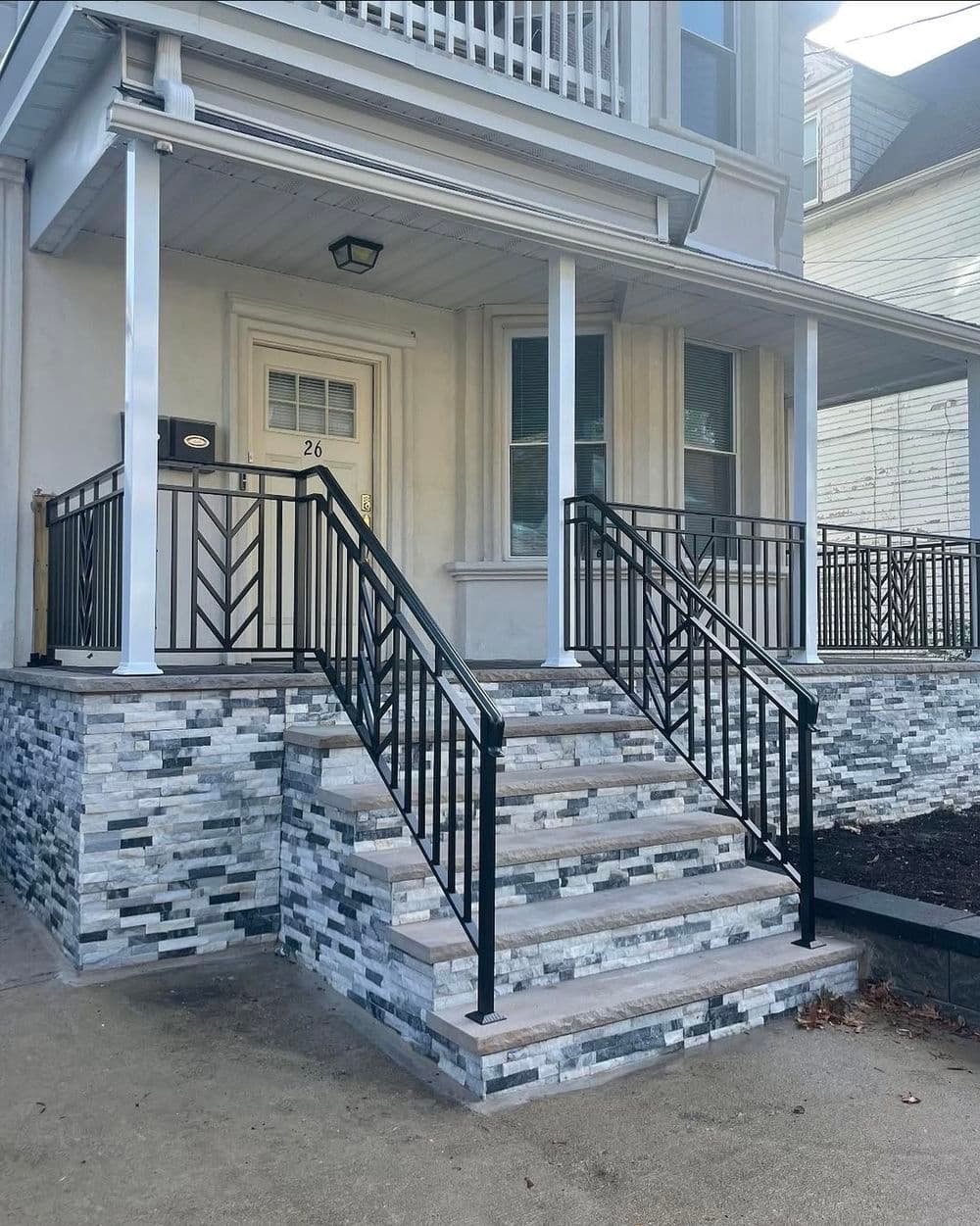 Modern home entrance with black metal railings and stone-patterned steps.