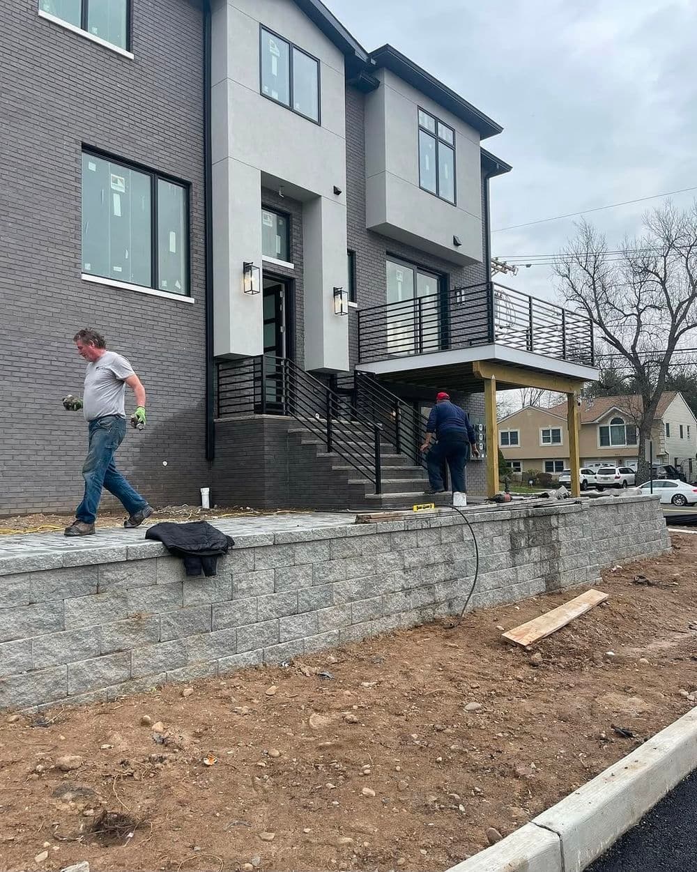 Construction workers at a modern home with a stone retaining wall and new landscaping.