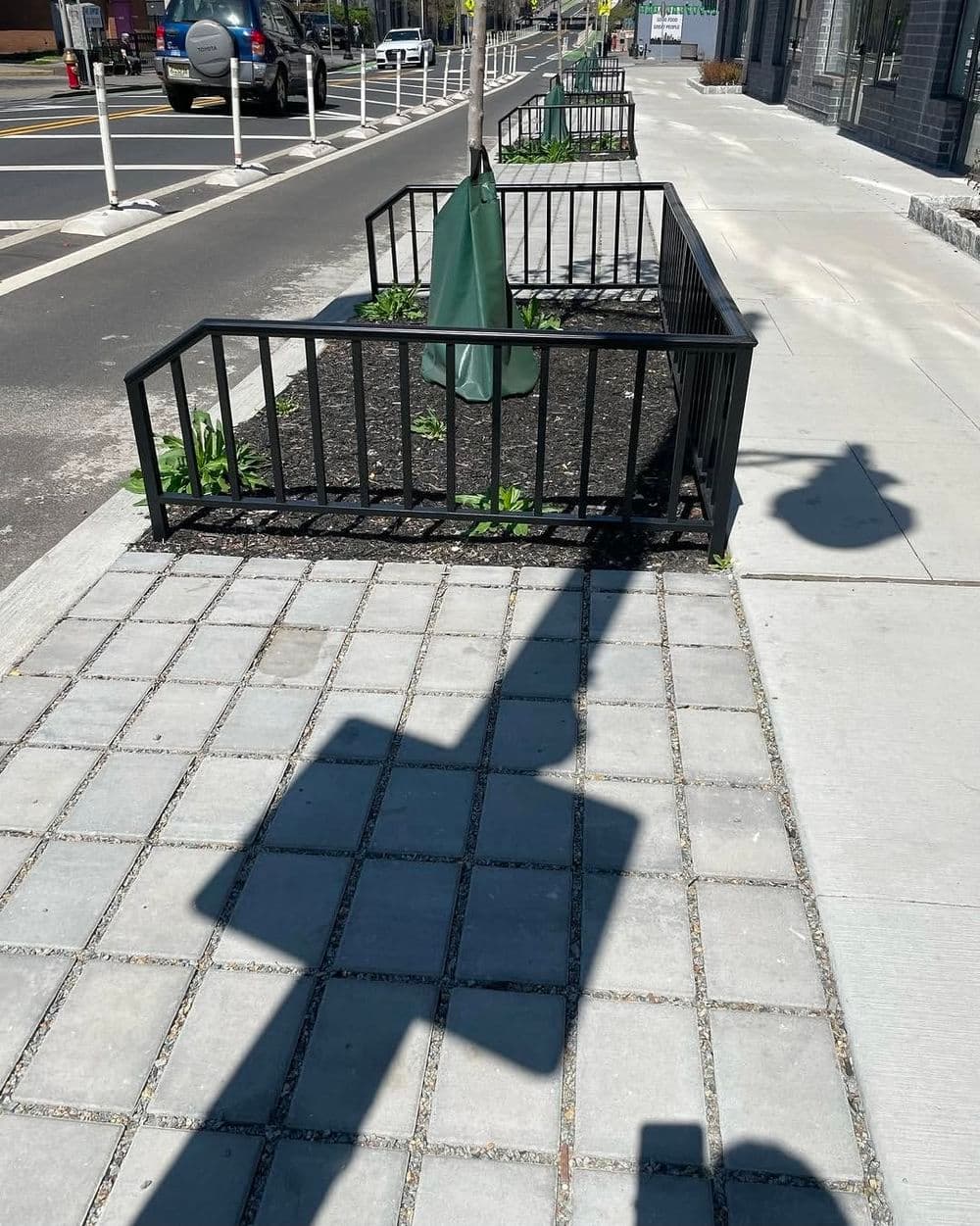 Urban streetscape with planters, shadows, and pedestrian walkway in a city setting.