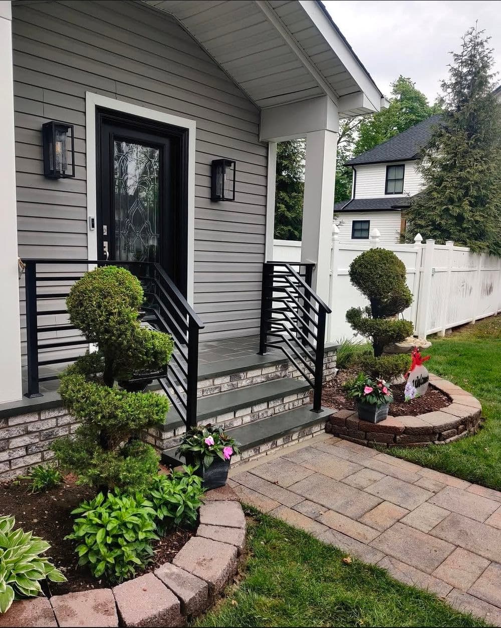 Decorative entrance with trimmed bushes, bright flowers, and modern railing design.