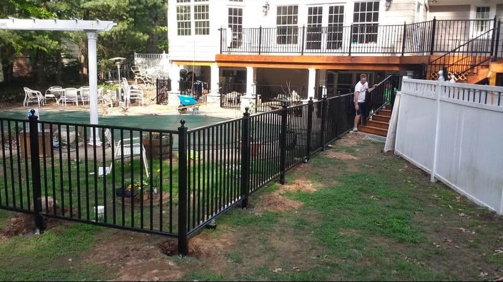 Black metal fence enclosing a backyard pool area with a deck and seating arrangements.