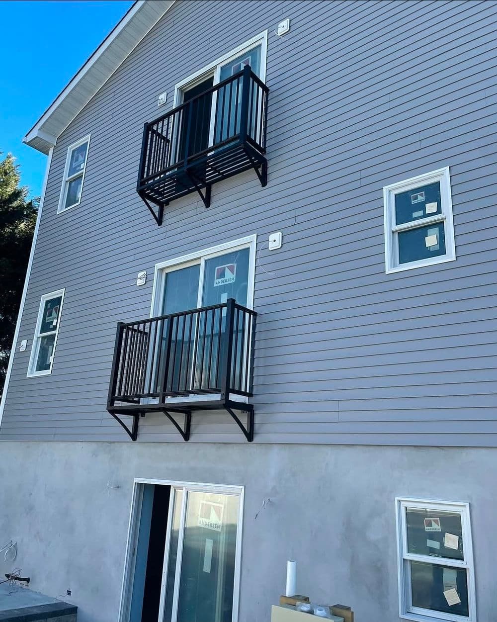 Modern building exterior with two balconies, gray siding, and large windows.