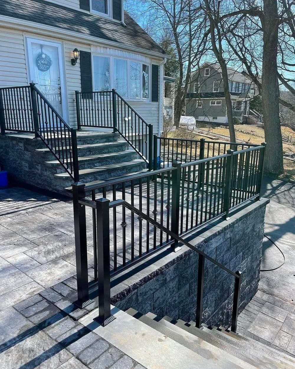 Black metal railing and stairs leading to a house entrance with a sunny backdrop and clear sky.