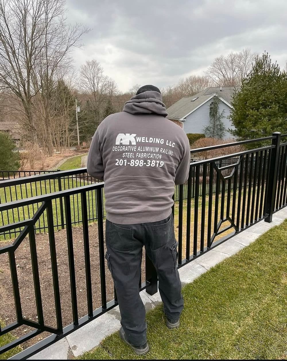 Welding LLC worker installing decorative aluminum railing in residential yard.