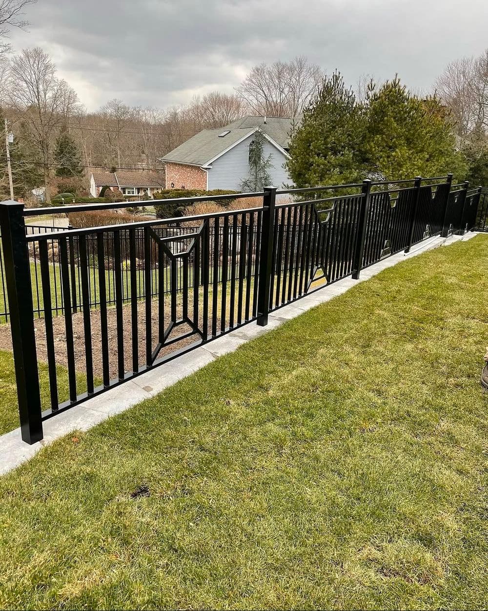 Black metal fence along a grassy yard with trees and a house in the background.