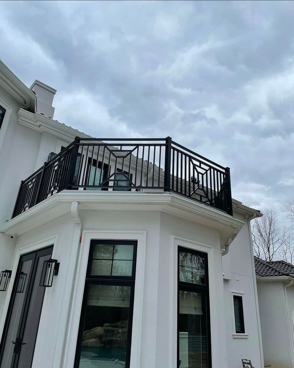 Modern home with black balcony railing under a cloudy sky. Elegant architectural details.