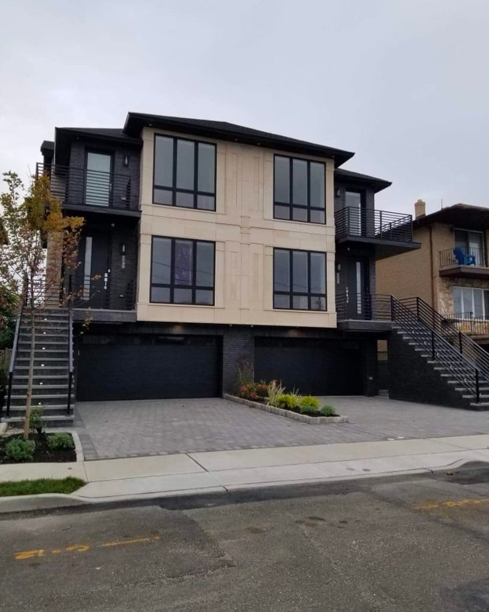 Modern two-family home with large windows and a sleek exterior, featuring stone accents and a paved driveway.