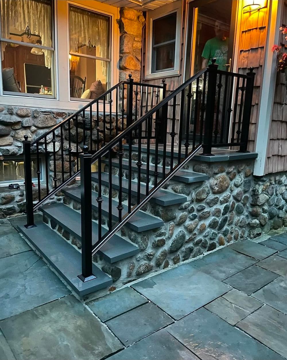 Black metal railing on stone steps leading to a cozy porch with warm lighting.