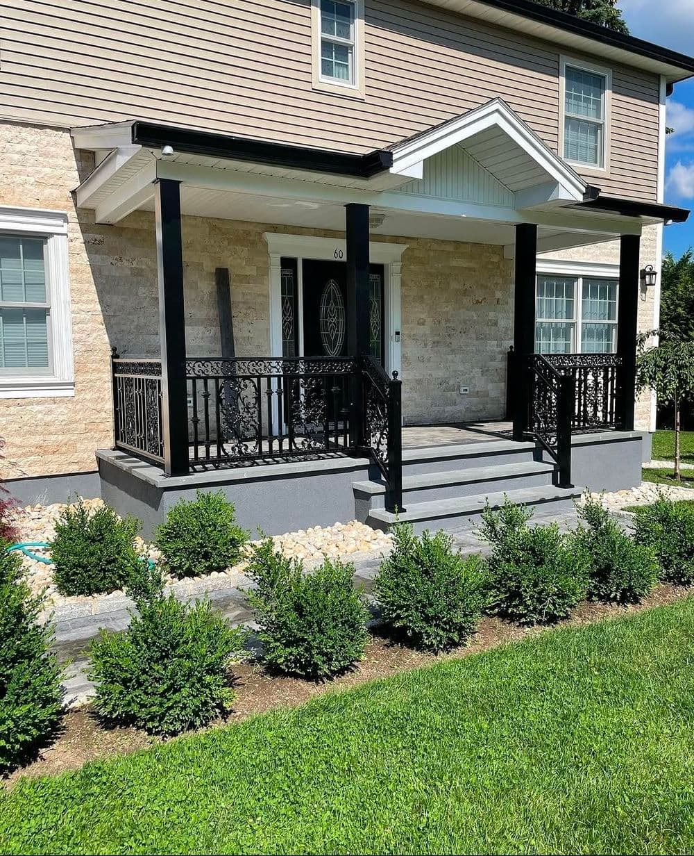 Modern home entrance with black railing, stone steps, and well-maintained landscaping.