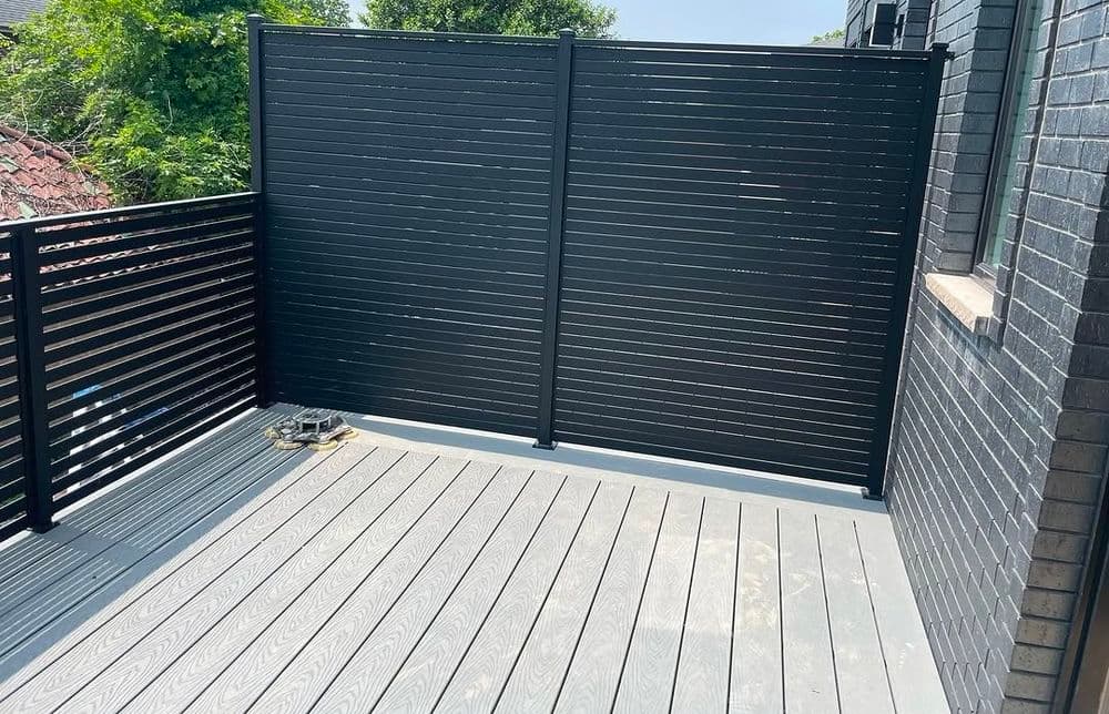 Modern balcony with black vertical slat privacy screen and gray wooden flooring.
