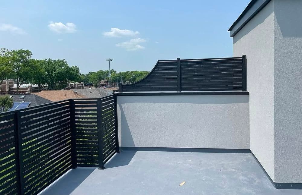 Modern rooftop balcony with black railing, overlooking a suburban neighborhood and blue sky.