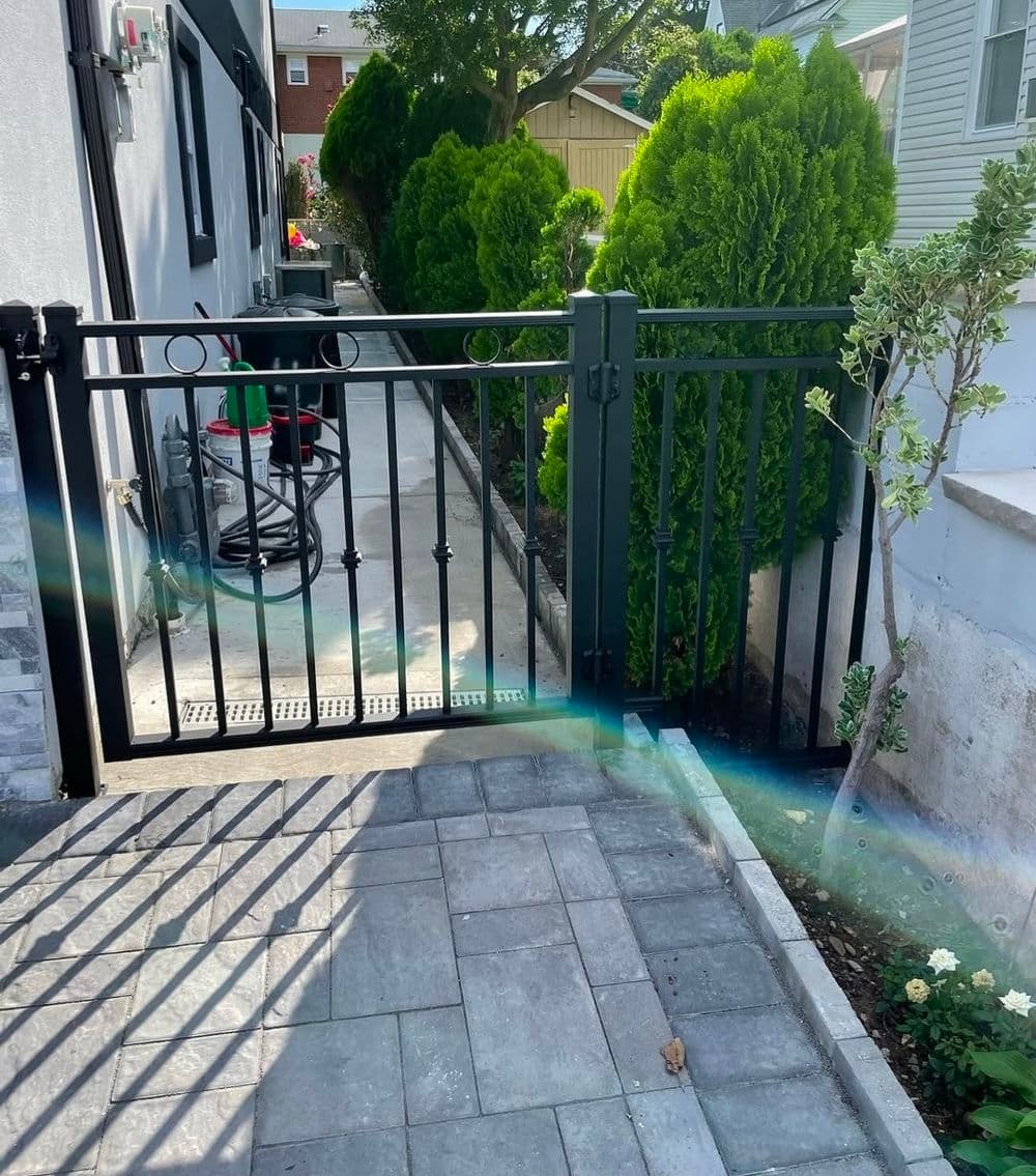 Black metal gate leading to a paved walkway and neatly trimmed hedges in a residential garden.