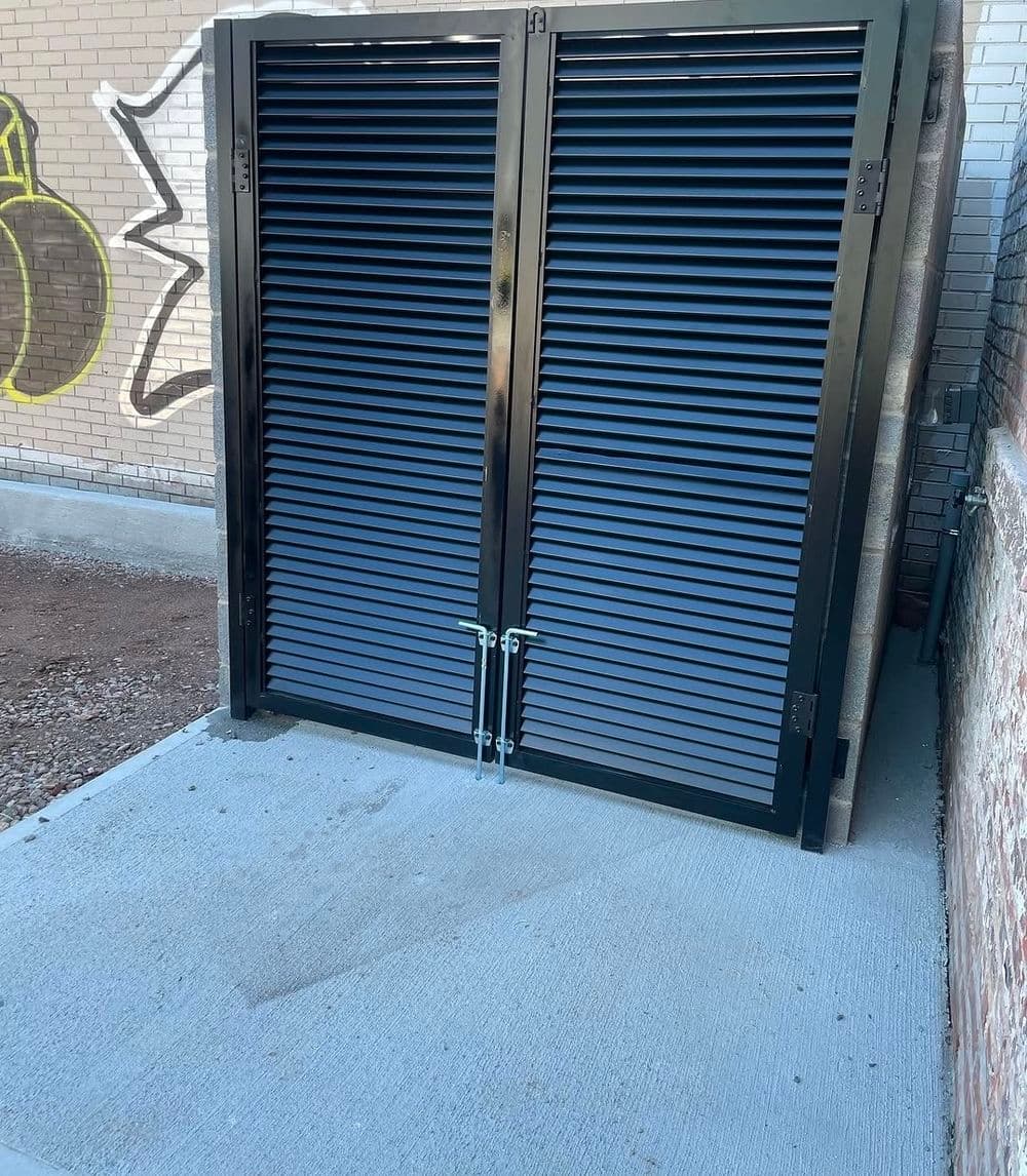 Black security gates with vertical slats installed against a brick wall.