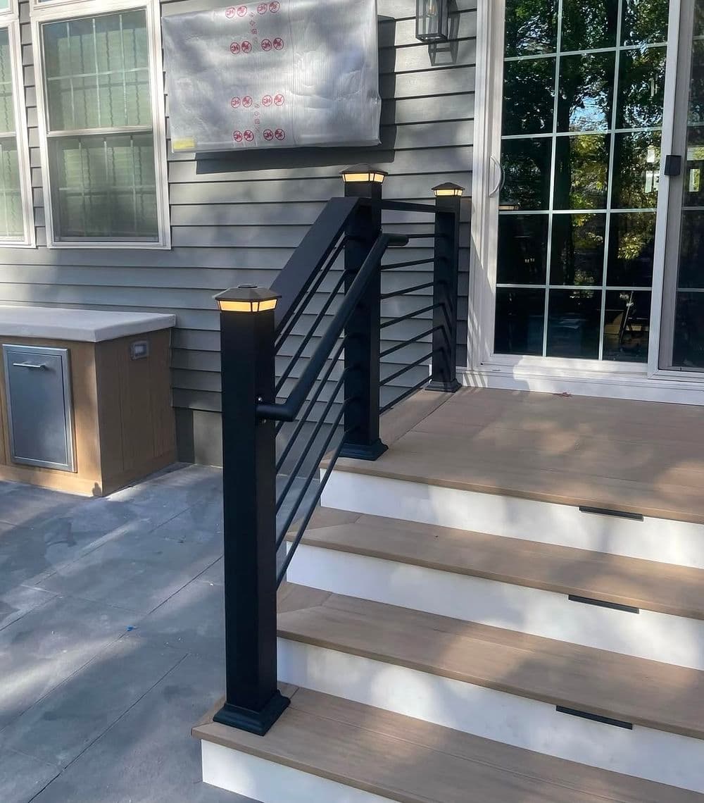 Modern outdoor staircase with black railing and illuminated posts leading to a patio.