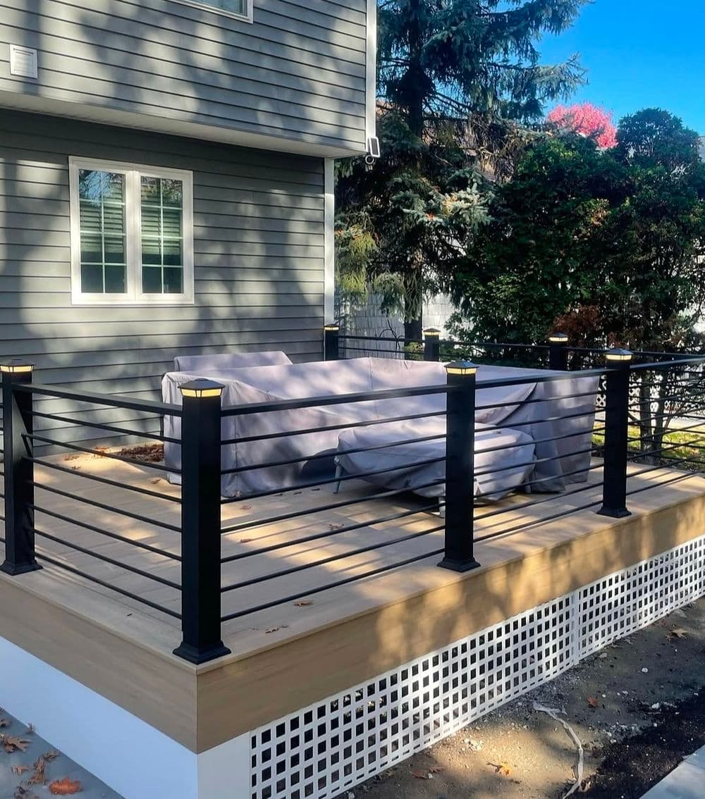 Modern deck with black railing, covered furniture, and landscaped surroundings. Bright sunny day.