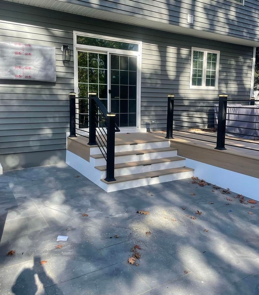 Modern home entrance with black railings, wooden steps, and gray siding.