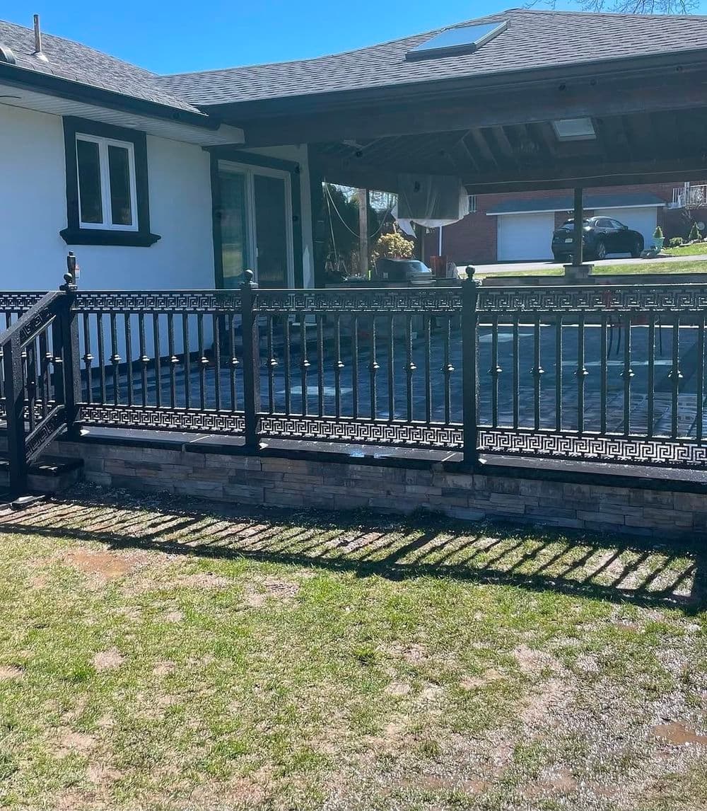 Black iron railing and stone wall surrounding a patio area behind a house on a sunny day.