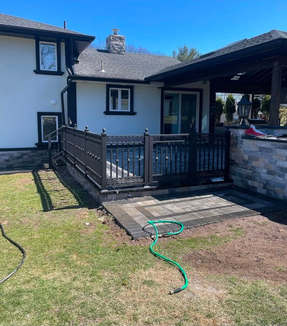 Newly installed patio with black railing and stone details beside a modern home.