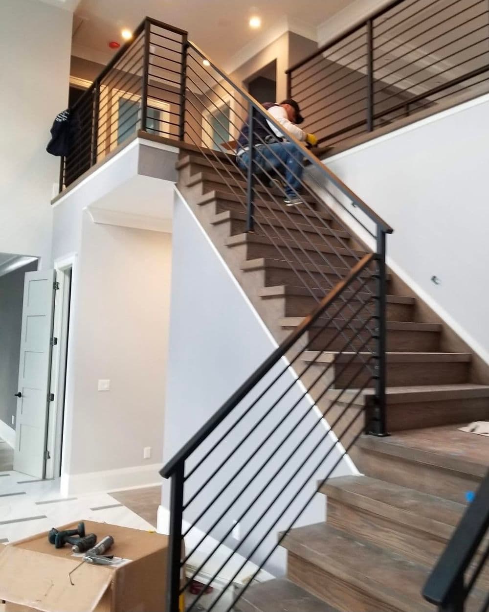 Modern staircase with sleek metal railing and a worker installing finishes indoors.